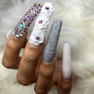 Long white nails with silver glitter and 3D flowers.
